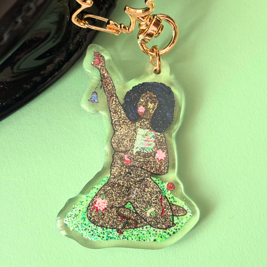 Keychain attached to a bag, of woman reaching up with flowers growing from her body.