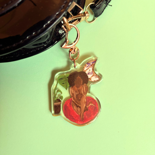 Decorative keychain with a person in a room with a plant and moon window