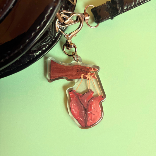 Keychain of hand controlling a heart with puppet strings attached to black bag